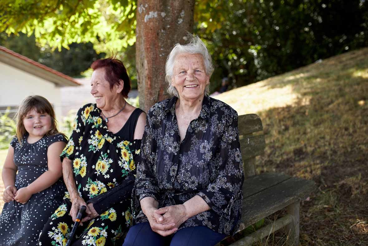 Foto: Zwei alte Frauen und ein junges Mädchen sitzen auf einer Bank und lächeln