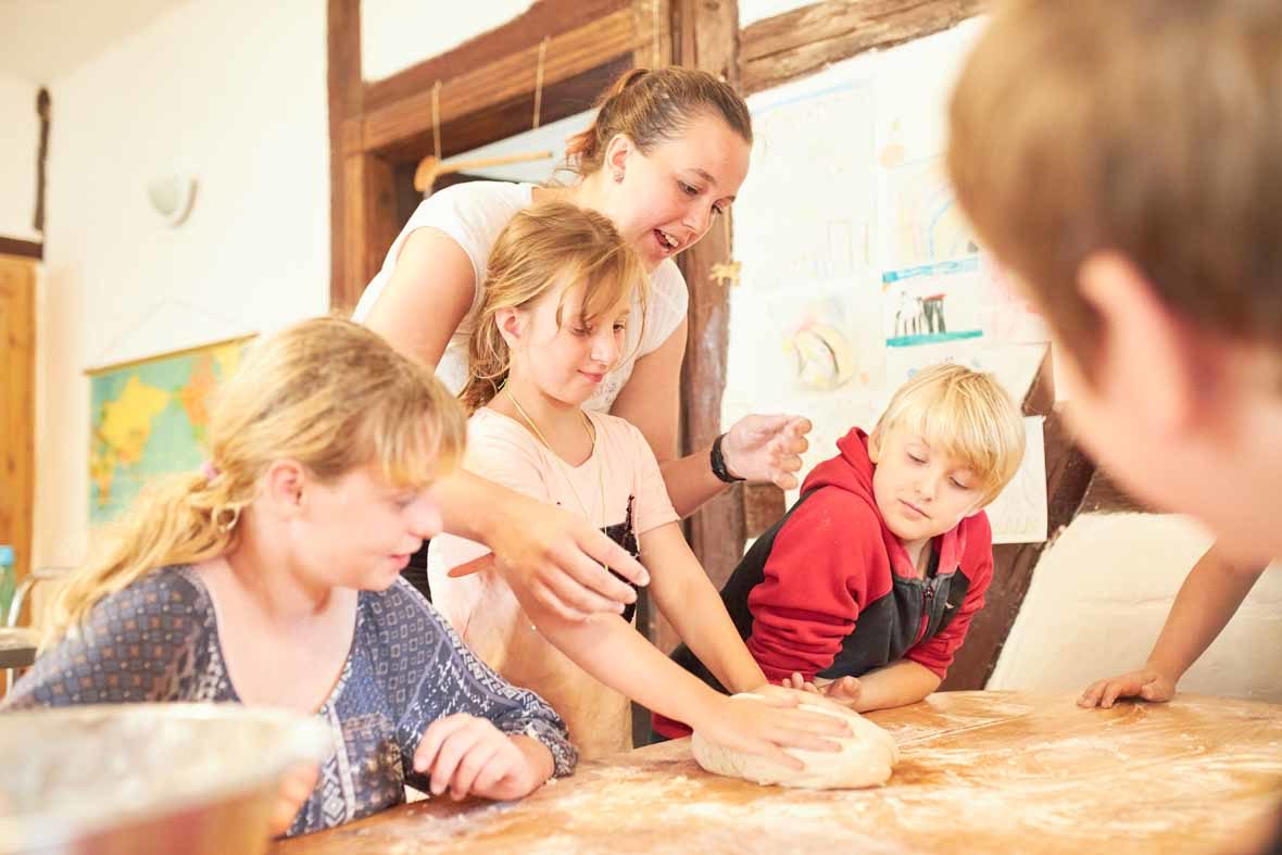 Foto: Ein Mädchen formt ein Brötchen aus Teig, andere Kinder schauen ihm zu