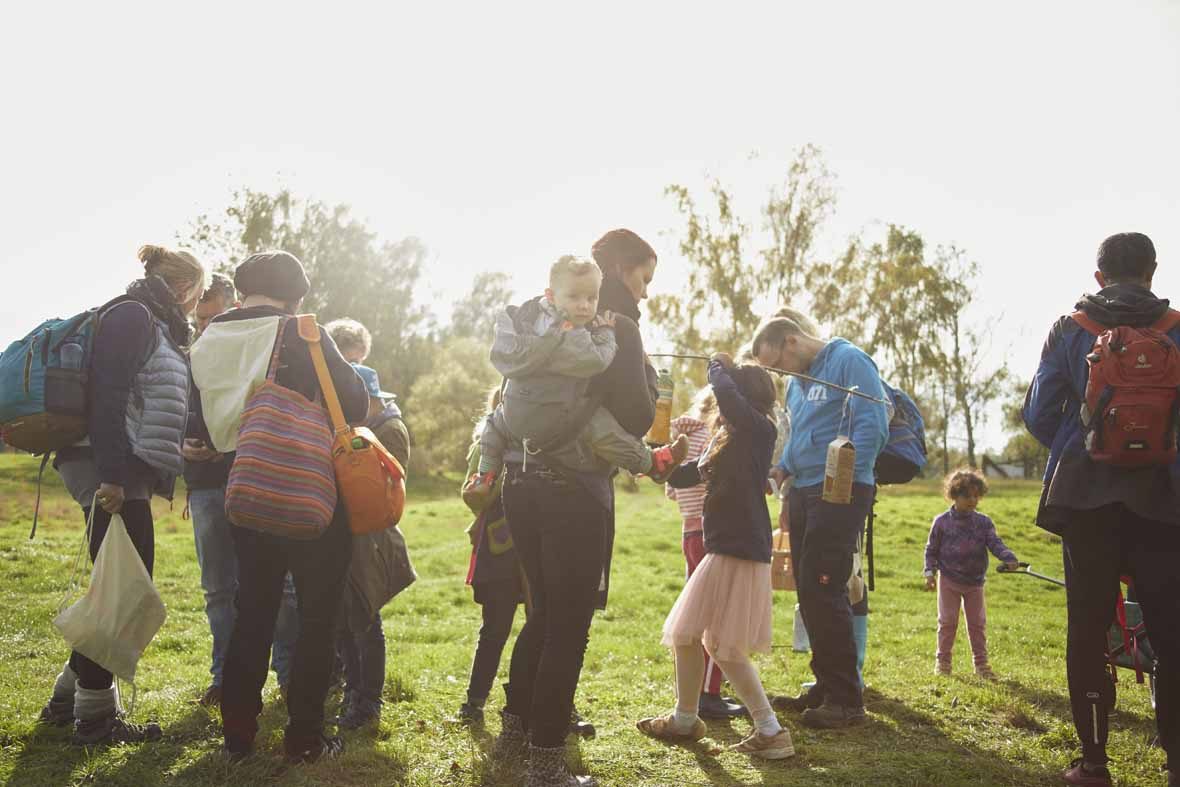 Foto: Eine Gruppe von Erwachsenen und Kindern mit Rucksäcken stehen auf einer Lichtung.
