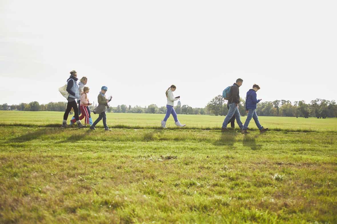 Foto: Eine Gruppe Erwachsene und Kinder gehen über eine Wiese.