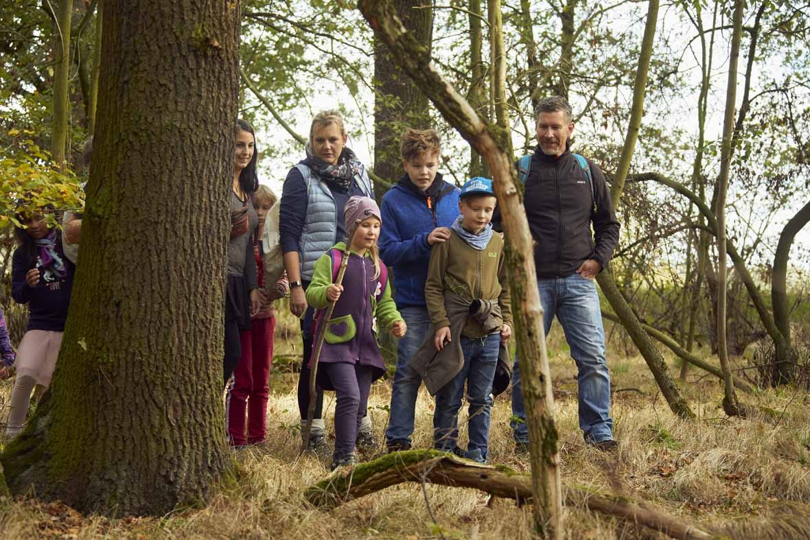 Foto: Eine Gruppe Erwachsene und Kinder laufen durch den Wald.