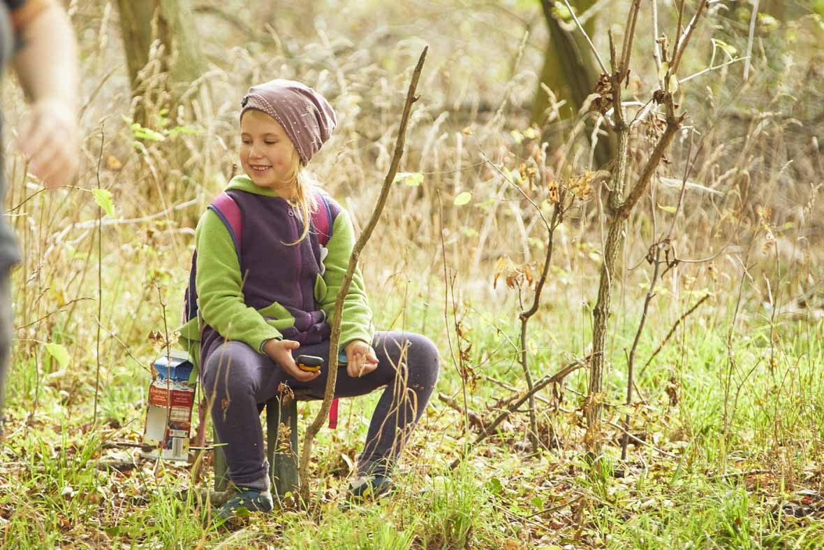 Foto: Ein Mädchen sitzt im Wald und lächelt.