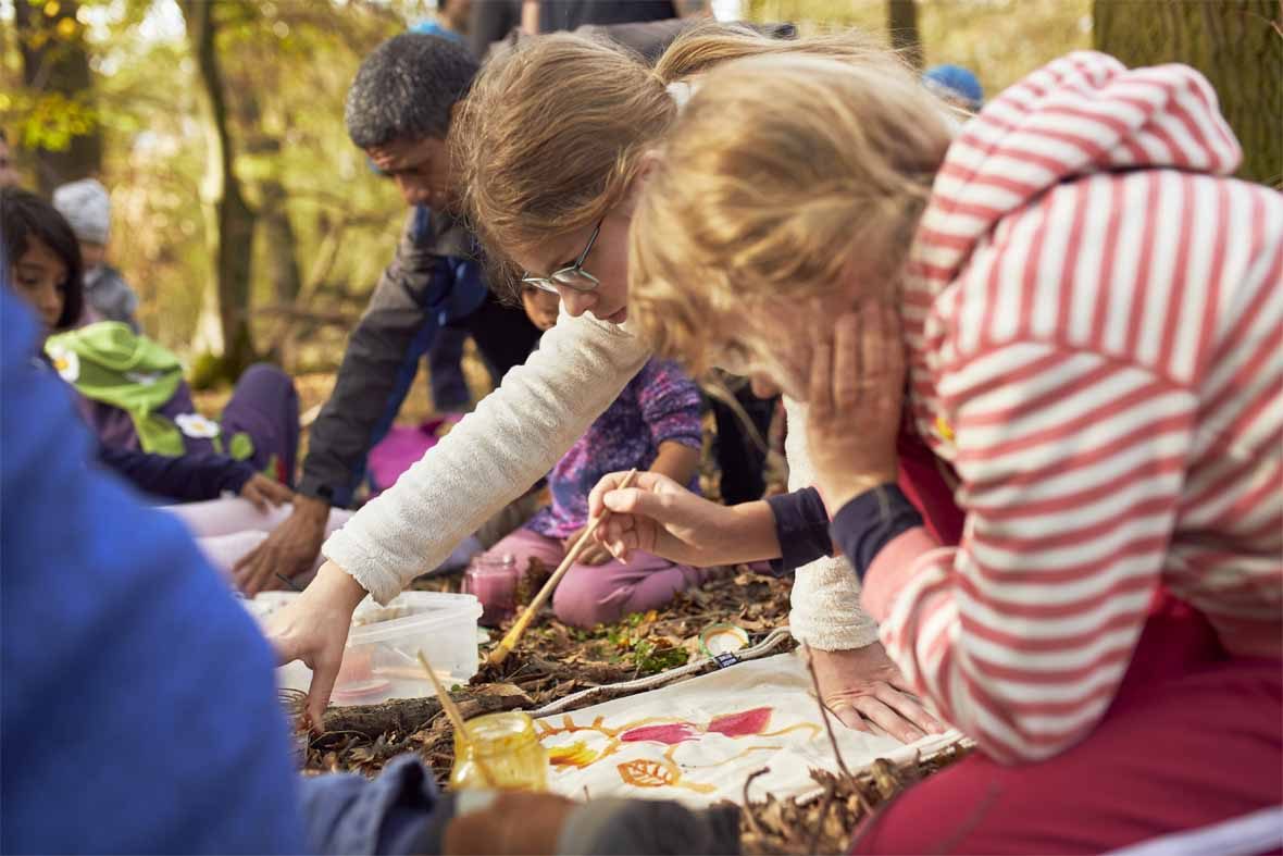 Foto: Auf dem Waldboden liegen Jutebeutel, die von Kindern bemalt werden.