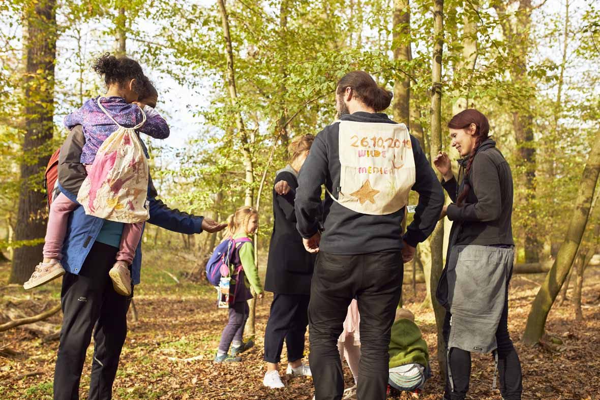 Foto: Eine Gruppe Menschen im Wald mit bemalten Jutebeuteln auf dem Rücken.