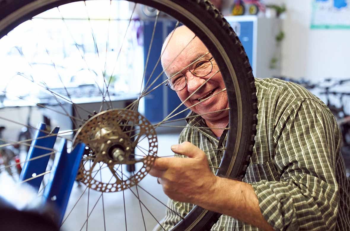 Ein Mann hält ein Fahrrad-Rad in der Hand und lacht