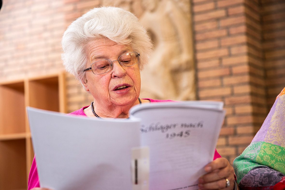 Eine ältere Frau blickt auf ein Gesangbuch und singt.