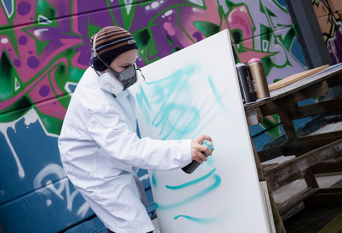 Ein June sprayt mit blauer Farbe auf eine Leinwand.