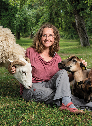 Andrea Göhring sitzt auf der Wiese und streichelt ein Schaf und eine Ziege