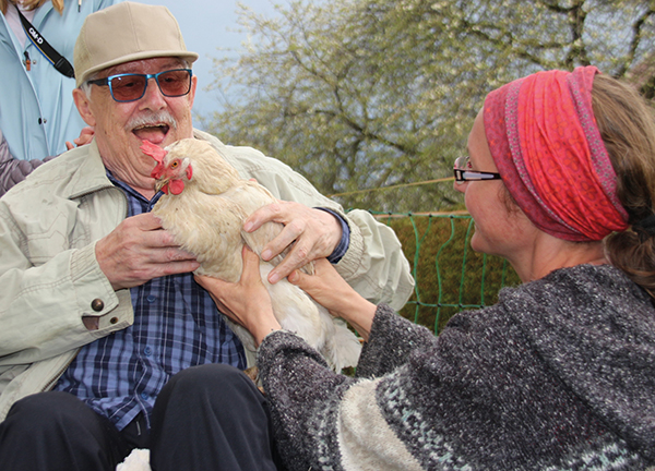 Ein älterer Herr hält ein Huhn in der Hand und lacht