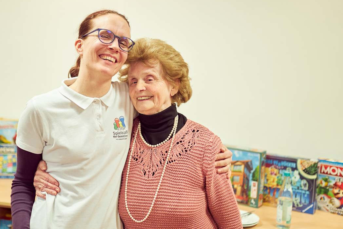 Petra Fuchs mit einer älteren Frau im Arm, im Hintergrund sind Brettspiele