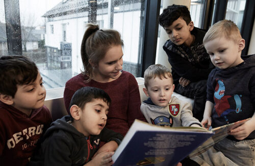 Eine Frau liest mehreren Kindern aus einem Buch vor, die Kinder schauen interessiert in das Buch hinein.